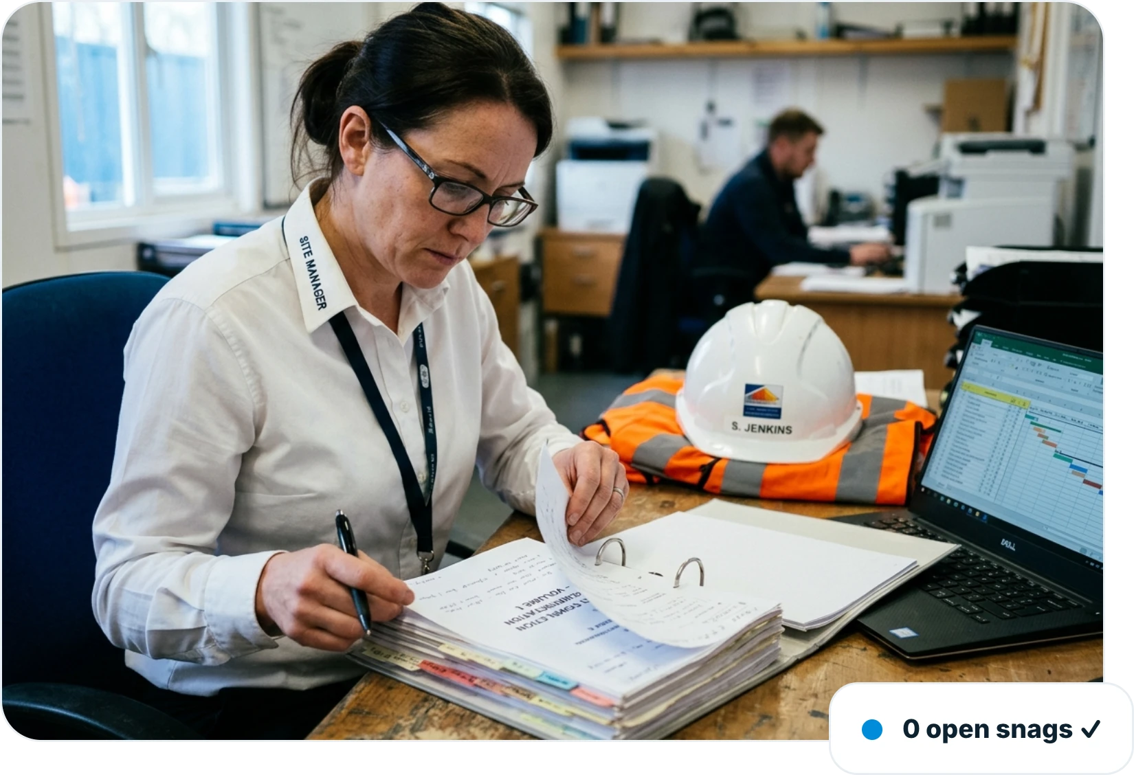 Project manager reviewing a completion document pack beside a laptop in a site office, with no open snags left on the plot