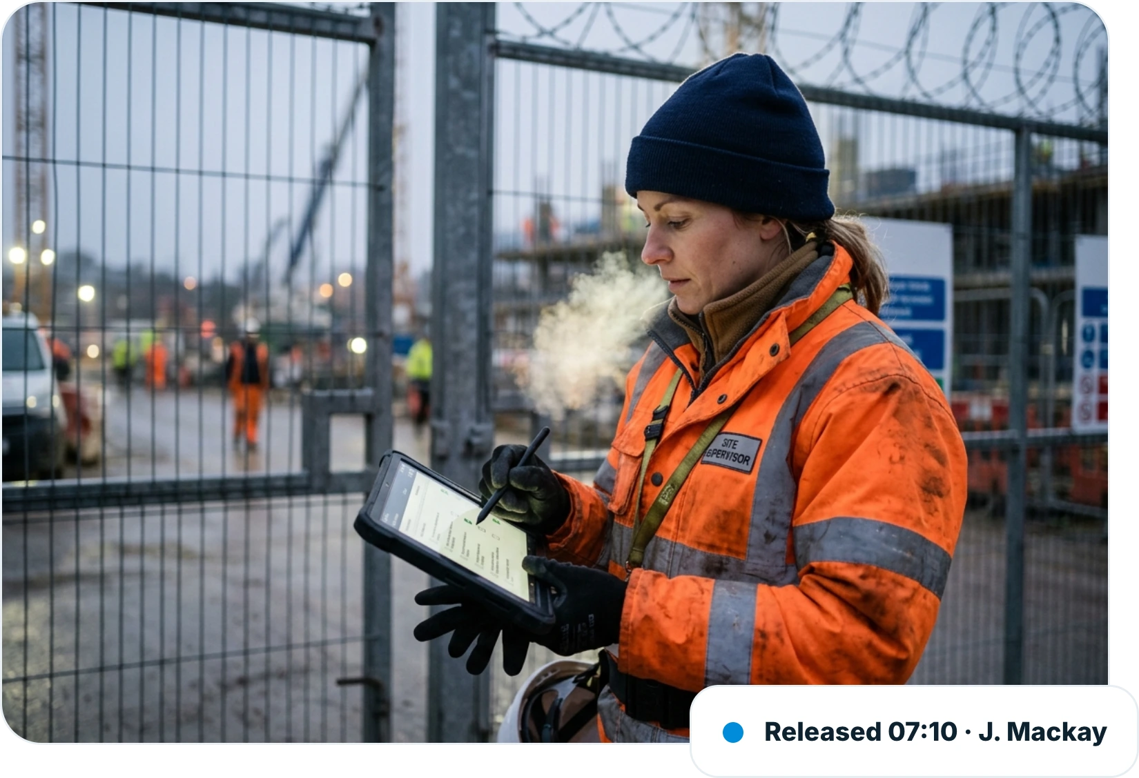 Site supervisor in a hi-vis jacket completing a pre-start checklist on a tablet at the site gate on a cold morning