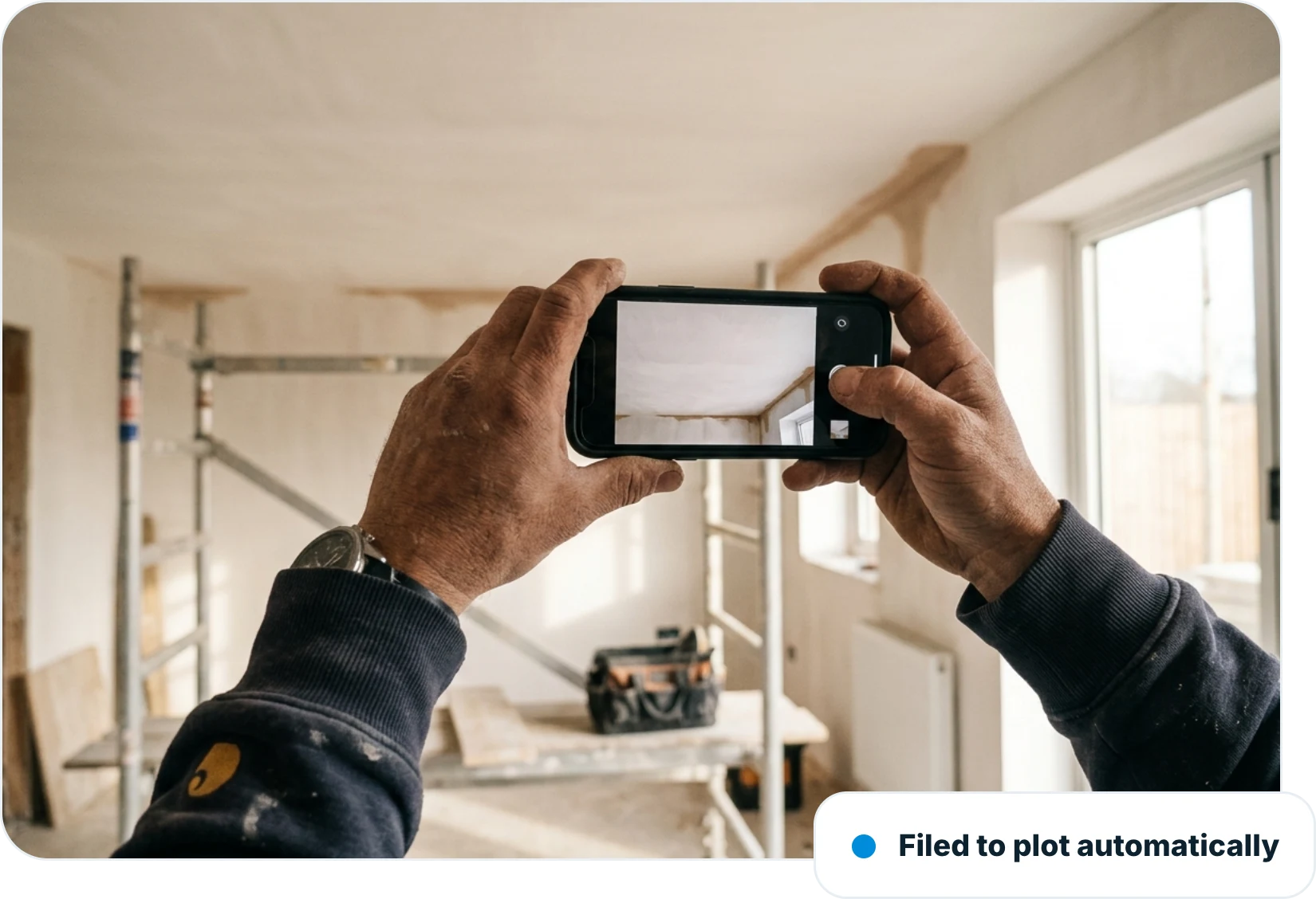 Hands photographing a newly plastered ceiling in a new-build room with a smartphone, filed to the plot automatically